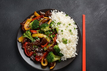 Asian teriyaki beef with red and yellow bell peppers, broccoli and sesame seeds on a plate on the...