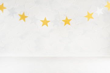 Festive scene with gold and silver glittering stars as garland hanging on string in soft light white abstract interior. Empty stage for design, showing, presentation of produce.