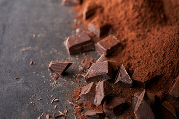 Pieces of dark chocolate and heaps of cocoa powder on dark stone underground