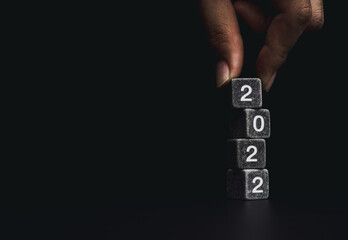 2022 Happy New year with the business goal concept. Hand putting a black dice on the top of the...