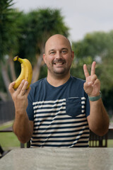 Man showing bananas while gesuring number two with hands outdoors