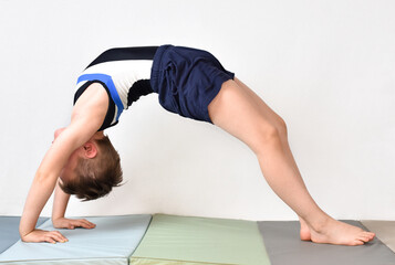 Little boy gymnast making bridge pose on white background