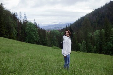 Fototapeta na wymiar Woman traveler standing on a glade high in the mountains in front of forest, space for text, atmospheric epic moment