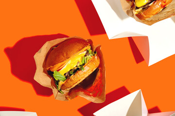 Big burger with cheese in a package on a bright orange background. Fast food delivery. Top view.