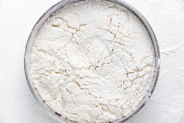 Flour in round metal bowl and scattered around on background. Flour texture background.