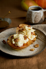 Baked halved pear with ricotta cheese, walnuts, honey and coffee. Tasty autumn dessert. Sweet rustic fruit with nuts on ceramic plate on wooden background. Healthy vegetarian food. Vertical side view