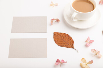Composition with gray paper business card, brown beech autumn leaves, hydrangea flowers and cup of coffee. mockup on white background. side view, copy space.