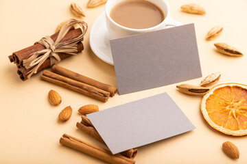 Fototapeta na wymiar Composition of gray paper business cards, almonds, cinnamon and cup of coffee. mockup on orange background. side view, copy space.