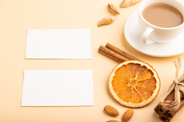 Obraz na płótnie Canvas Composition of white paper business cards, almonds, cinnamon and cup of coffee. mockup on orange background. side view, copy space.
