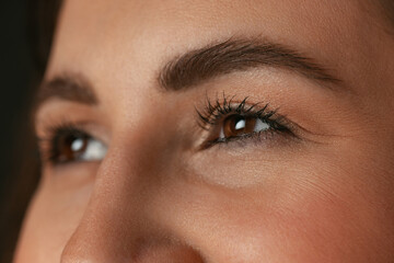 Close-up image of female brown eyes without makeup isolated over dark studio background. Natural beauty concept.