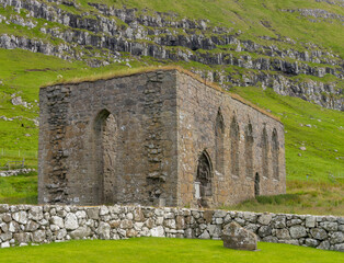 Fototapeta na wymiar The ruins of St. Magnus Cathedral in Kirkjubøur (Kirkebø) a historical village on Streymoy, Faroe Islands. The ruins are the largest medieval building in the Faroe Islands.