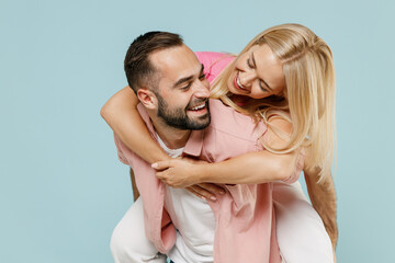 Young fun couple two friends family man woman in casual clothes giving piggyback ride to joyful, sit on back together isolated on pastel plain light blue background studio People lifestyle concept