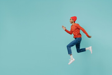 Full body side view fun cool young smiling happy african american man in orange shirt hat jump high run fast isolated on plain pastel light blue background studio portrait People lifestyle concept.