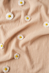 Flatlay of aesthetic Parisian styled background with chamomile flower buds on crumpled neutral beige muslin cloth. Flat lay, top view - obrazy, fototapety, plakaty