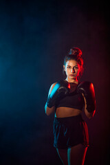Fototapeta na wymiar woman practicing boxing or kickboxing with colored lights and smoke