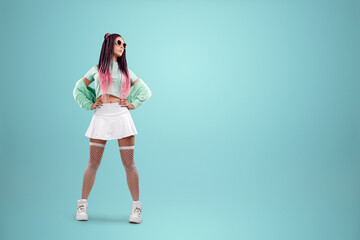 Millennial girl with pink braids hairstyle in turquoise clothes and sunglasses posing on a blue background. Concept for modern style, inclusiveness, individuality, generation Z, copy space.