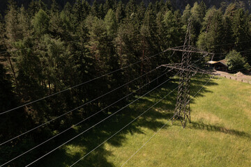 Transmission tower and power lines over the field close to the forest.