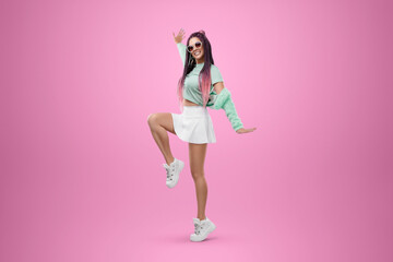 Millennial girl with pink braids hairstyle in turquoise clothes and sunglasses posing on a pink background. Concept for modern style, inclusiveness, individuality, generation Z, copy space.