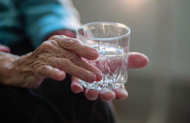 A glass of water in the wrinkled hands of an elderly woman, grandmother drinks water, health care,...