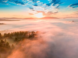 Fog spreads over the mountains at dawn. The sun rises on the horizon. Ukrainian Carpathians in the morning. Aerial drone view.