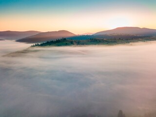 Fototapeta na wymiar Fog spreads over the mountains at dawn. The sun rises on the horizon. Ukrainian Carpathians in the morning. Aerial drone view.