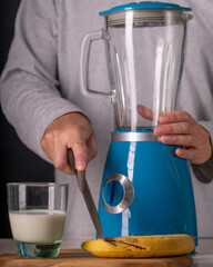 A man cuts a banana with a blender and a glass of milk nearby to make a smoothie