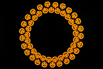 Orange pumpkins are arranged in a circle in two rows, forming a frame on a black background. Jack's lamp for a terrible holiday. Dark background with a place for Halloween text, for design. Top view.
