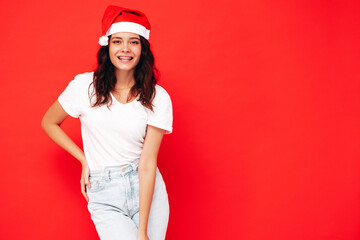 Beautiful woman celebrating New Year.Happy gorgeous female in casual clothes having fun at New Year's Eve party.Holiday celebration.Charming model in Santa Claus hat laughing near red wall