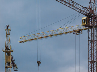 Yellow construction cranes against cloudy sky background.