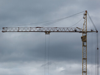 Yellow tower crane against cloudy sky background.