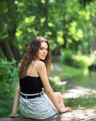 Fototapeta premium A woman in a denim skirt and a top is sitting on a log in the forest