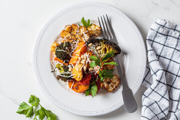 Mix of baked vegetables (broccoli, cauliflower, sweet potato and garlic) with cheese on white plate. Vegetarian healthy detox dinner.