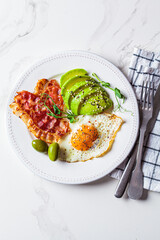 Keto breakfast concept. Fried egg with avocado and fried bacon in white plate.
