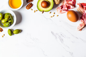 Keto diet ingredients frame on white marble background, copy space. Low carbohydrate menu concept.