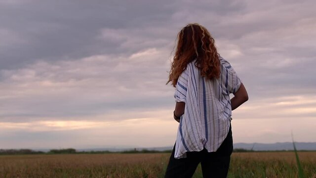 Shirtless woman admiring and reflecting on a landscape of a rice field as the breeze gives her.