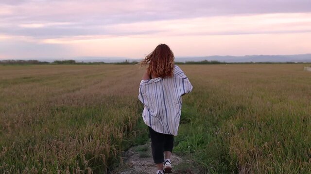 Woman in a shirt walking through a rice field while the breeze gives her.