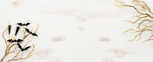 top view image of Halloween holoday. witcher broom, bare trees and bats over white wooden table