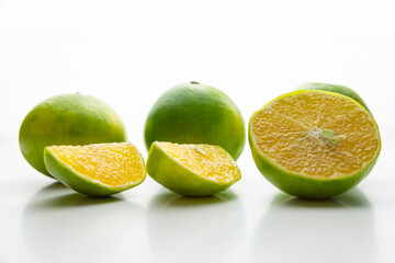 Ripe tangelos, and ripe tangelos cut in half, on a white surface, photographed against the light. 