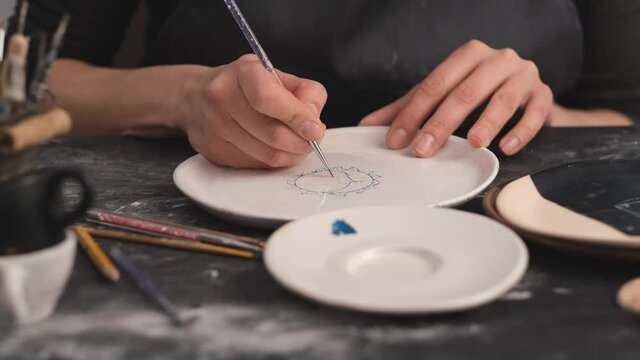 Woman hands during painting on ceramic plates. Potter workshop of making handcraft clay dishes