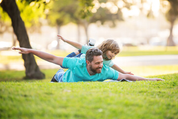 Father lying on grass, with excited happy little child son on shoulder. Carefree two man...
