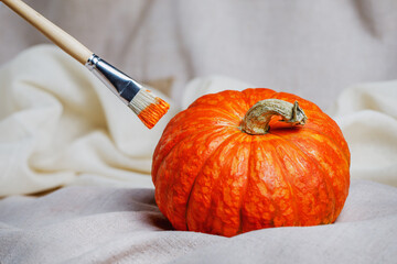 Artistic brush with orange paint and a beautiful ripe pumpkin lie on sacking. Preparing for...