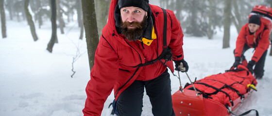 Mountain rescue service provide operation outdoors in winter in forest, injured person in stretcher.