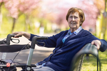 Seniorin sitzt allein im Park im Frühling auf einer Bank , den Rollator neben sich