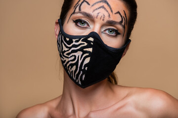 young model with tiger makeup and animal print mask looking away isolated on beige