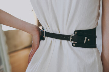 A slim girl in a white dress tries on a belt with black leather