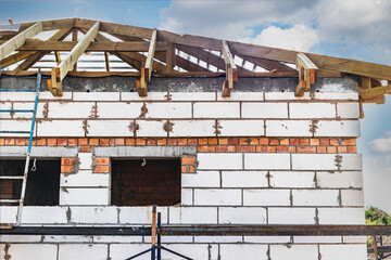Fototapeta na wymiar Building site of a house under construction. Unfinished house walls made from white aerated autoclaved concrete blocks. Wooden truss system.