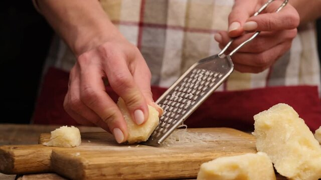 Woman grating pieces of parmesan cheese on wooden board