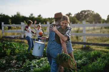 Happy mid adult female farmer hugging her senior friend holding basket with homegrown vegetables...