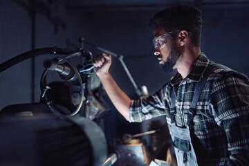 Fototapeta na wymiar Portrait of young concentrated african american industrial man working on cutter indoors in metal workshop.