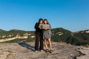 Cheerful businesswomen using laptop and tablet in nature